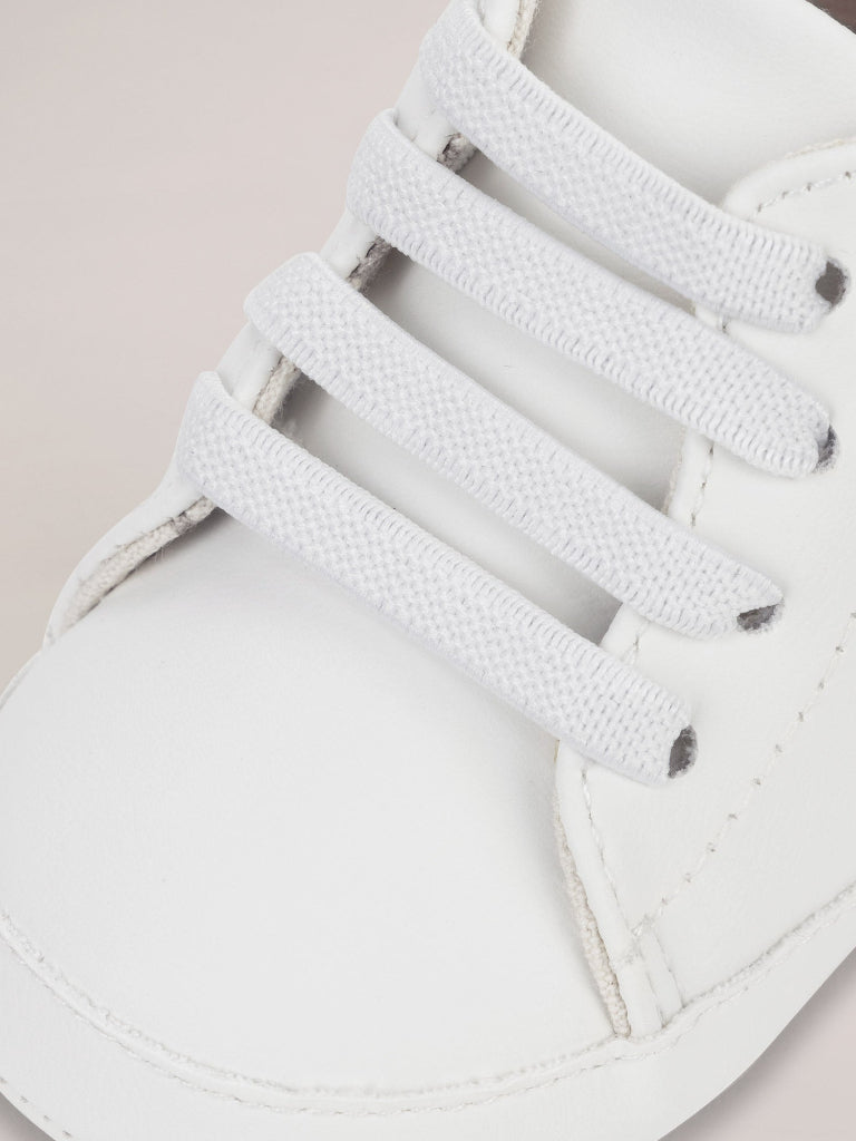 Close-up of white sneakers with laces on a light pink background