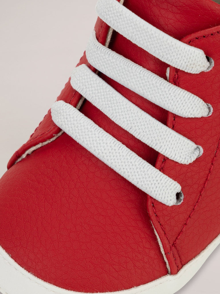 Red shoe with white laces on a light pink background