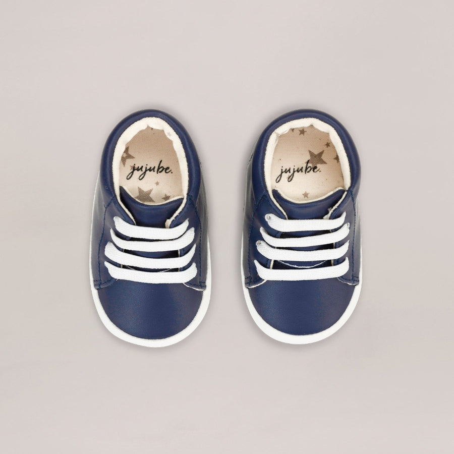 Pair of navy blue children's sneakers with white stripes on a gray background