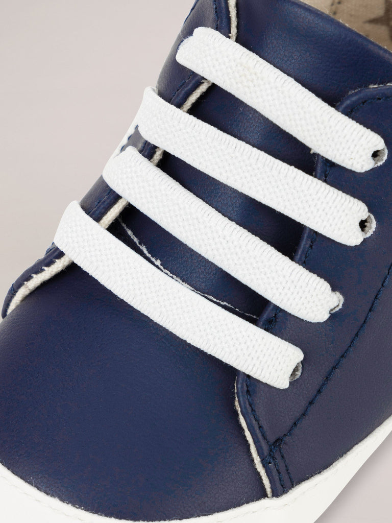 Navy blue shoe with white laces on a neutral background