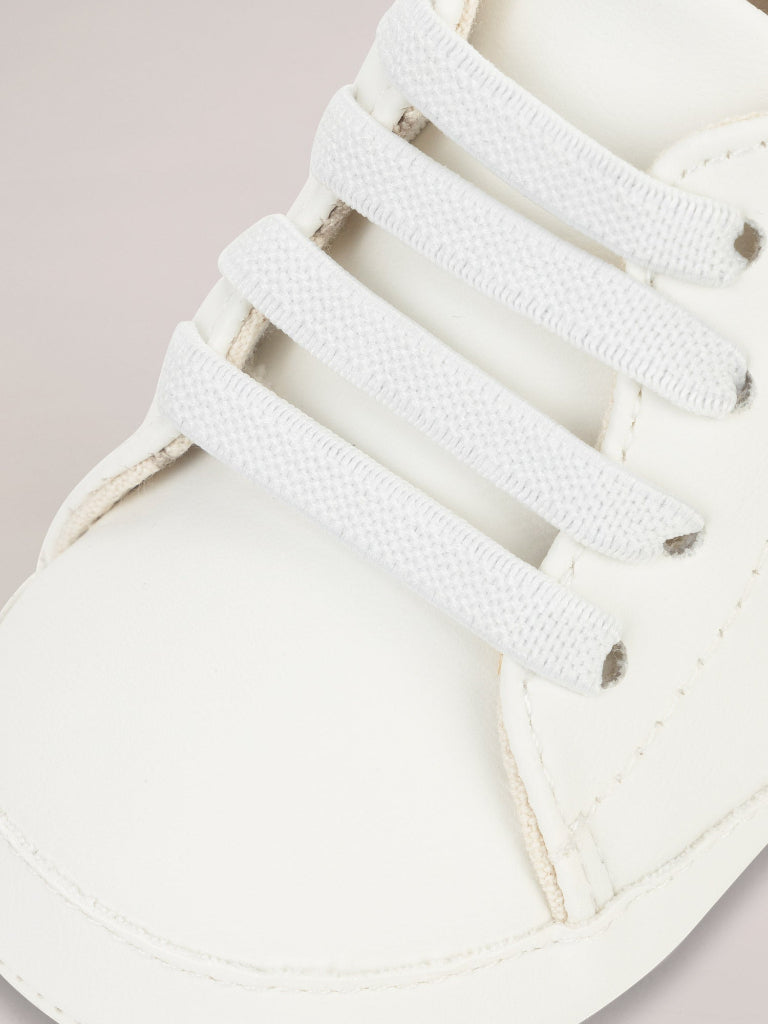 Close-up of white sneakers with laces on a light pink background