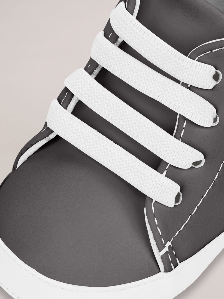 Close-up of a shoe with white elastic shoelaces on a neutral background