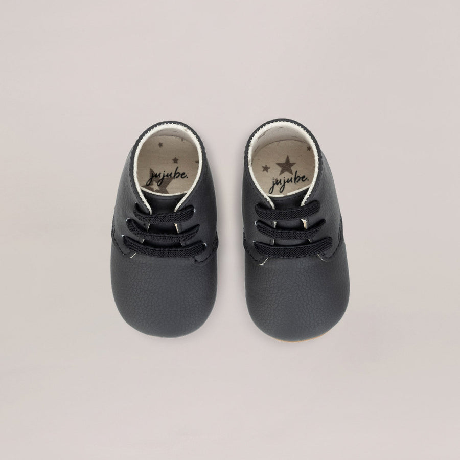 Pair of black baby shoes with 'ju-Ju-Be' branding on a light gray background