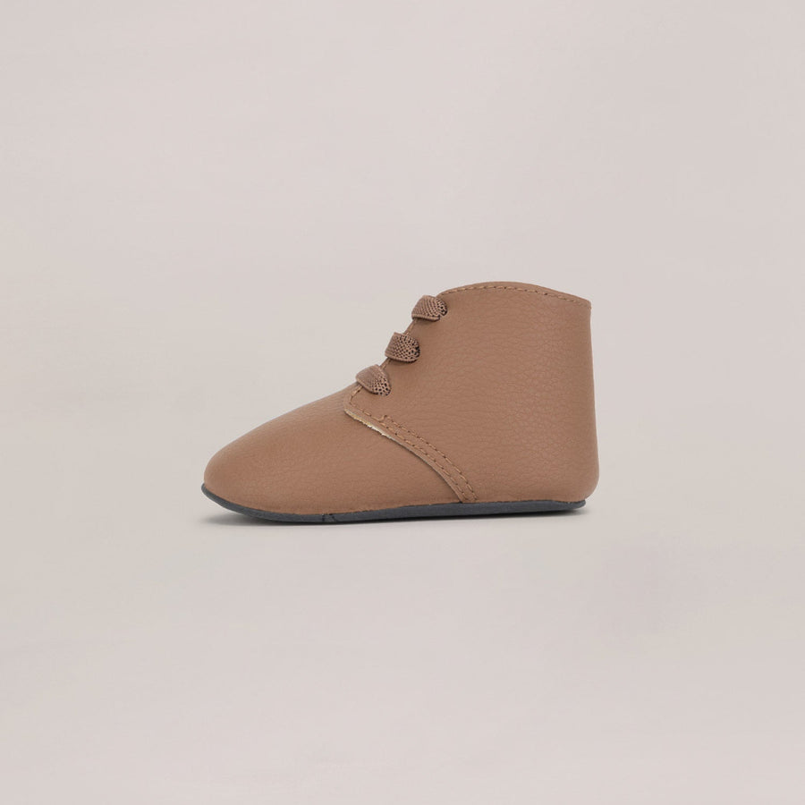 Brown baby bootie with a soft sole on a beige background