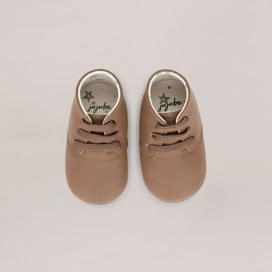 Pair of brown baby shoes with 'jujube' branding on a beige background