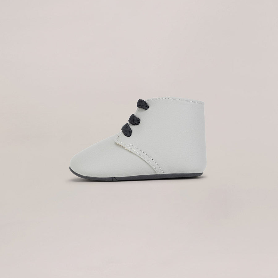 Light gray baby booties with black laces on a beige background