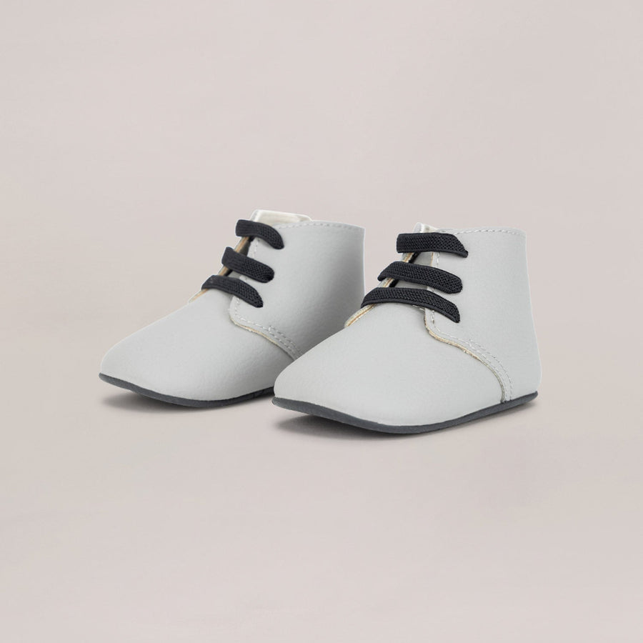 Pair of light gray baby shoes with black laces on a beige background