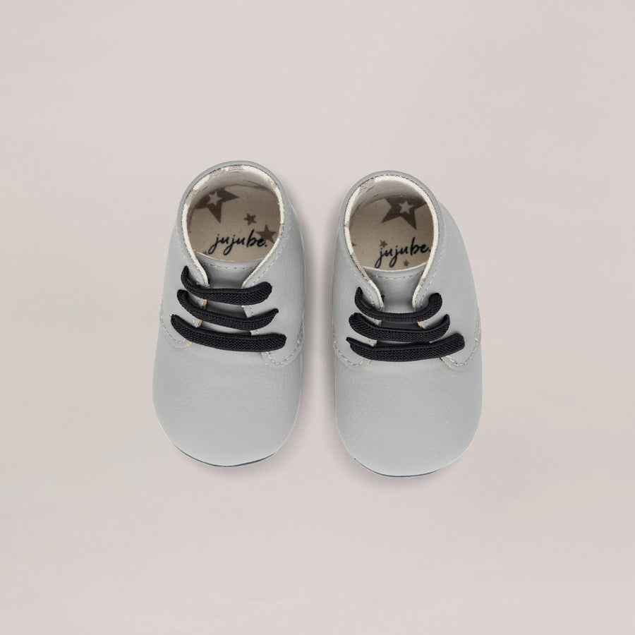 Pair of light gray baby shoes with black laces on a beige background