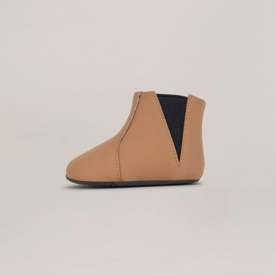 Tan ankle boot with black accent on a beige background