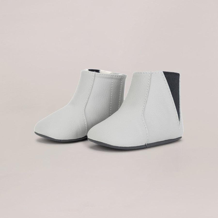 Pair of light gray ankle boots with a dark gray patch on a beige background
