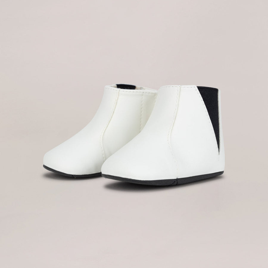 White ankle boots with black accents on a light beige background