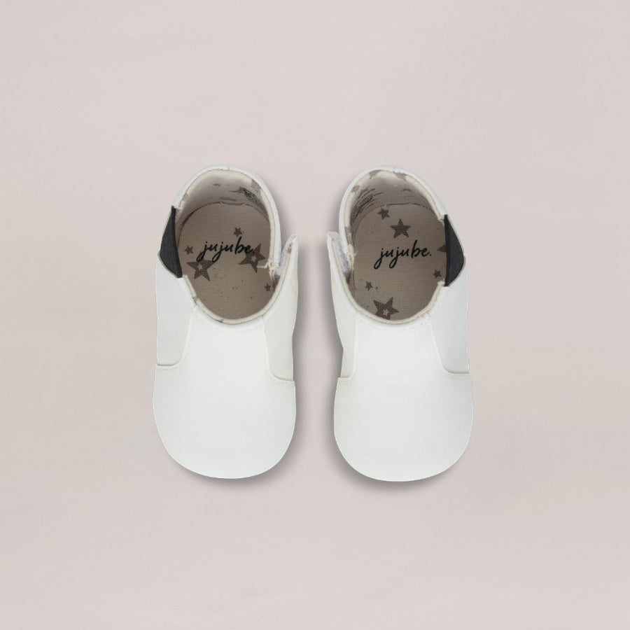 Pair of white baby shoes with black soles on a light pink background