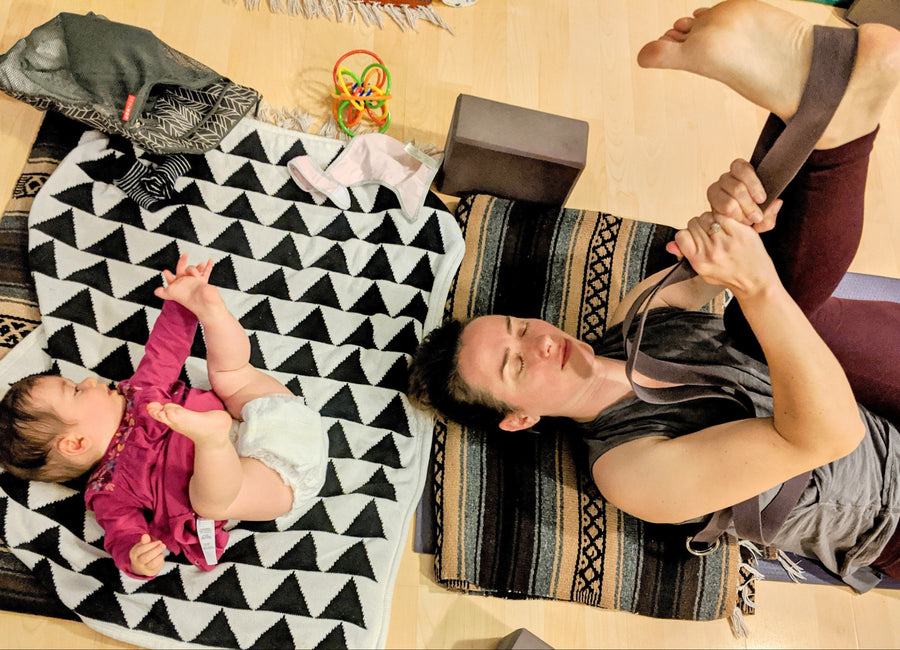 Woman doing yoga and baby lying on a patterned blanket. Both with feet in the air