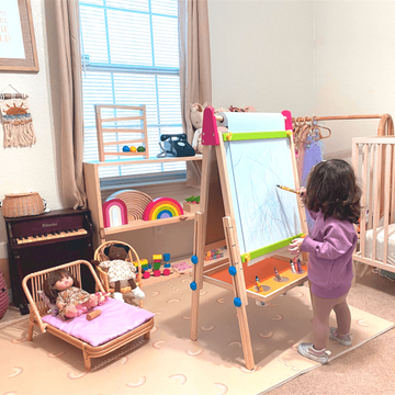 Child drawing on an easel in a child-friendly room with toys and furniture.