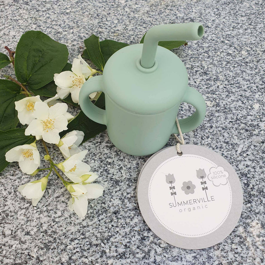 Light green silicone cup with straw on a gray surface with white flowers and a 'Summerville Organic' label.
