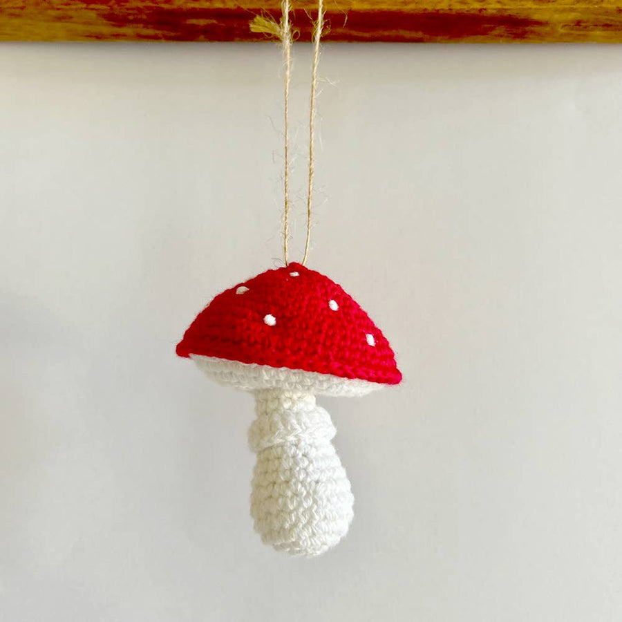 Crocheted mushroom ornament with red cap and white body on a plain background