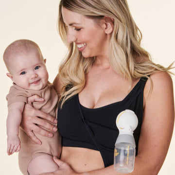 Woman holding a baby in nursing / pumping bra with  breast pump on a beige background
