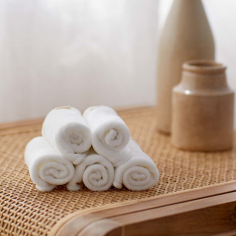 Stack of white towels on a woven surface with ceramic jars in the background