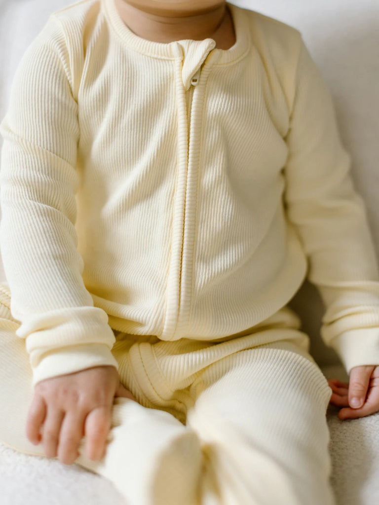 Baby wearing a cream-colored outfit sitting on a white surface