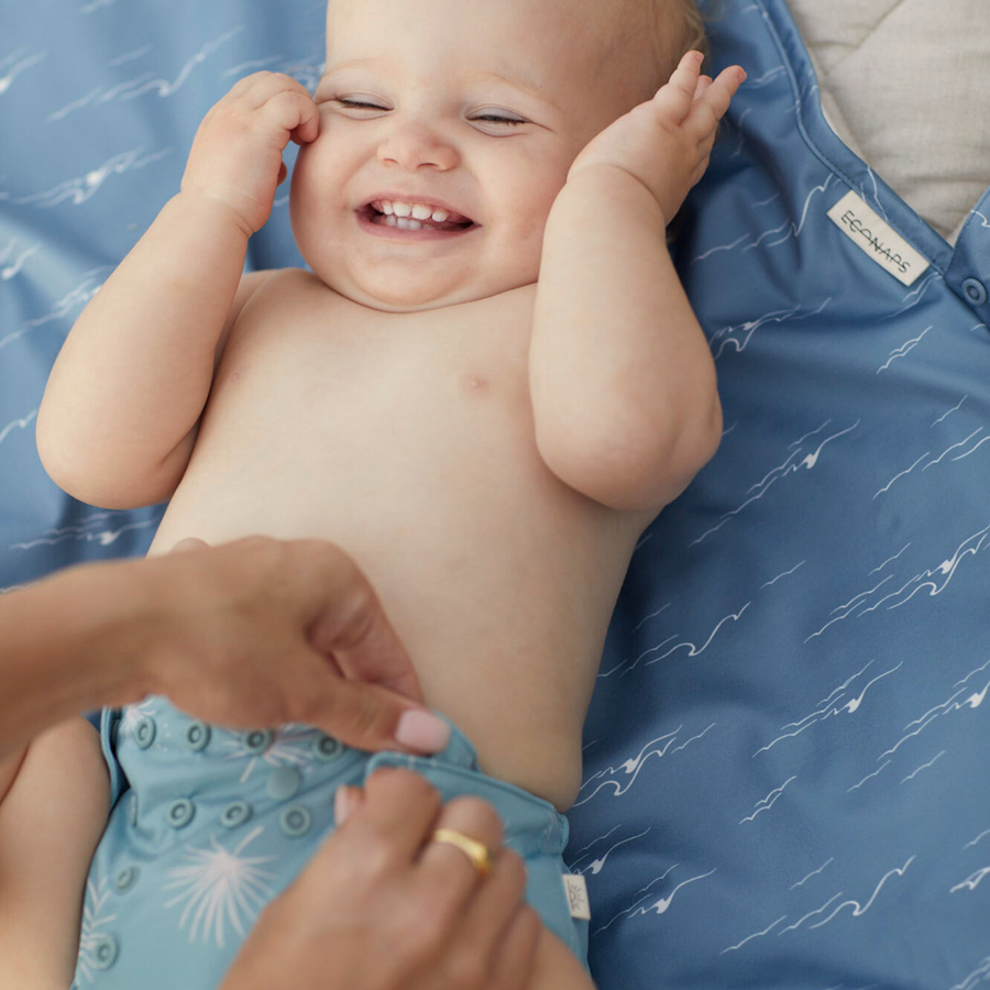 Baby lying on a blue mat with a person adjusting their diaper