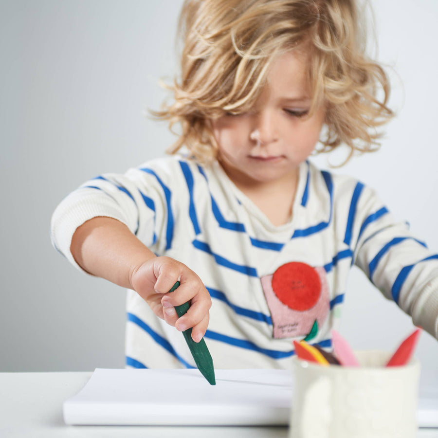 Child drawing with a green crayon on a white sheet of paper.