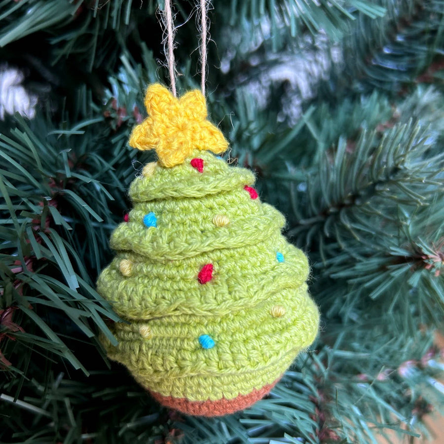 Crocheted Christmas tree ornament with a star on top, hanging on a tree.