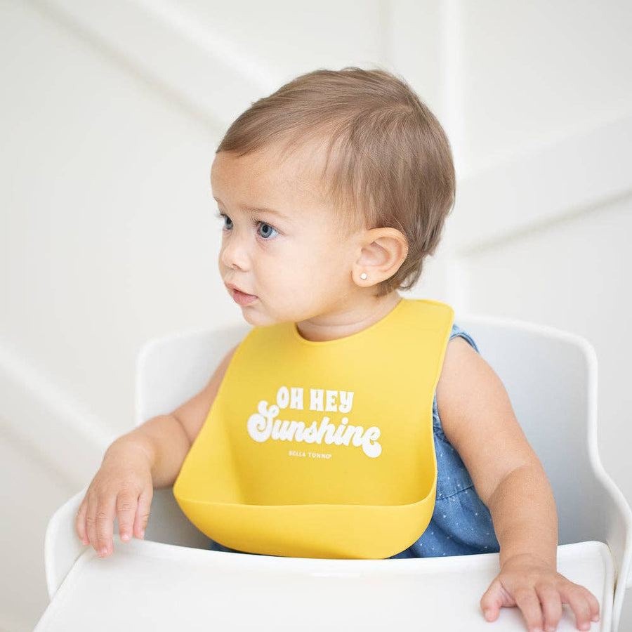 Baby wearing a yellow bib with 'Oh Hey Sunshine' text, sitting in a high chair.