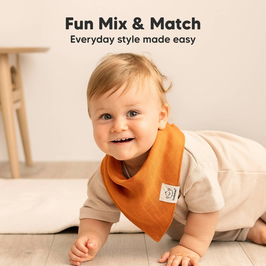 Baby wearing an orange bib with a visible brand logo, sitting on a light-colored floor.