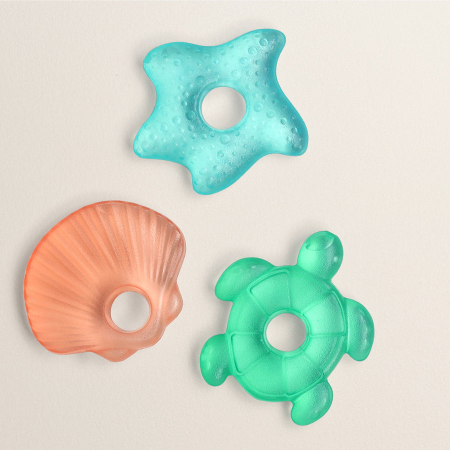 Three colorful baby teething toys shaped like a starfish, shell, and turtle on a beige background.