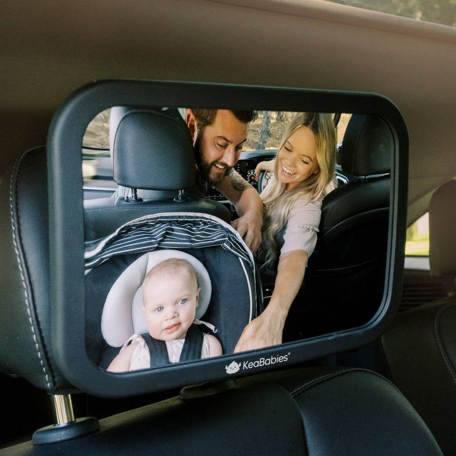 Car mirror with a baby in a seat and parents looking at it, brand 'KeaBabies' visible
