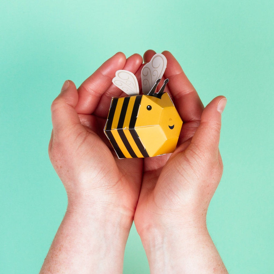 Image shows a pair of light skin toned child's hands cupping the buzzy bumble bee, against a light green background
