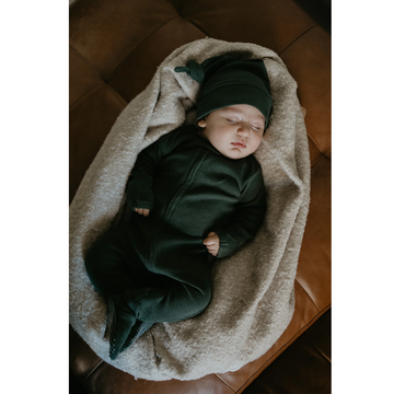 Newborn baby wrapped in a green outfit and hat on a brown blanket.