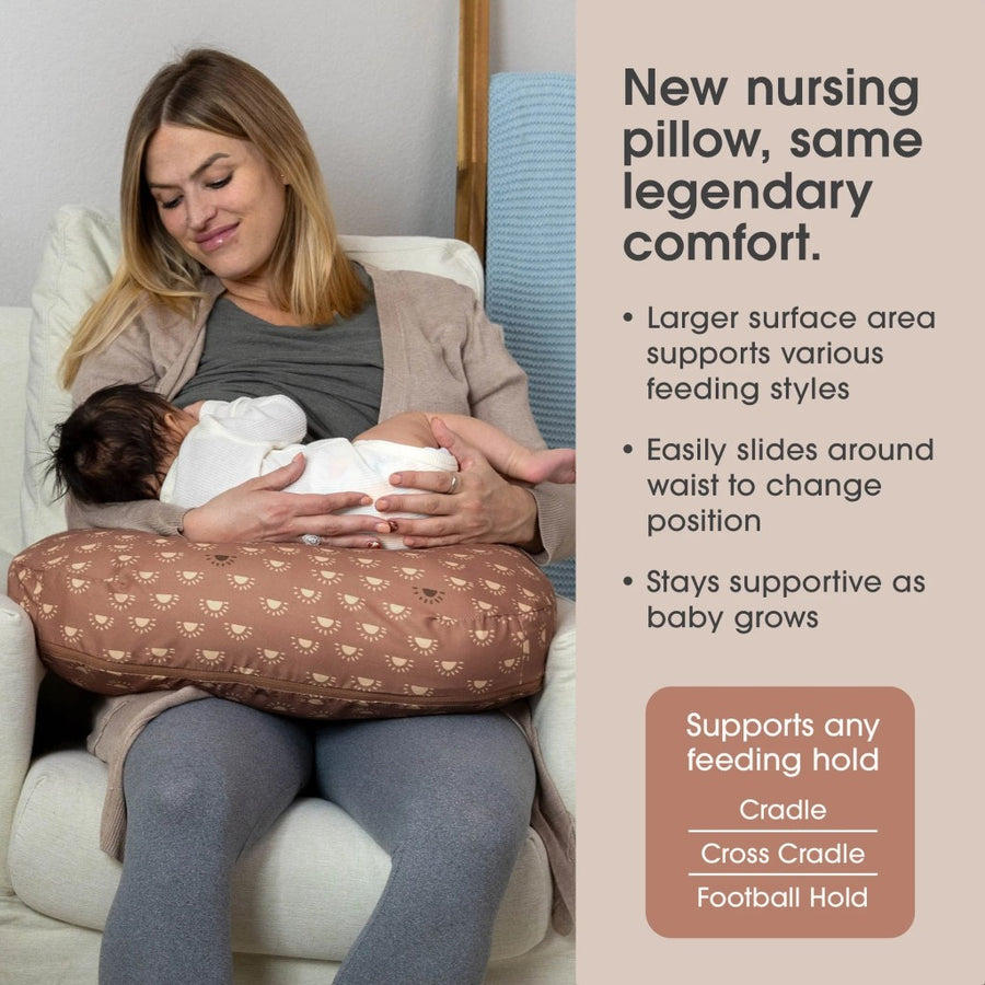 Woman holding a baby while using a nursing pillow with text about its features.