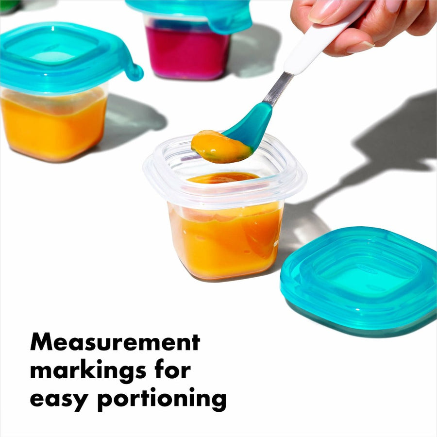 A light skinned hand is scooping orange puree out of a silicone baby block with a teal and white baby spoon, with text that reads, 