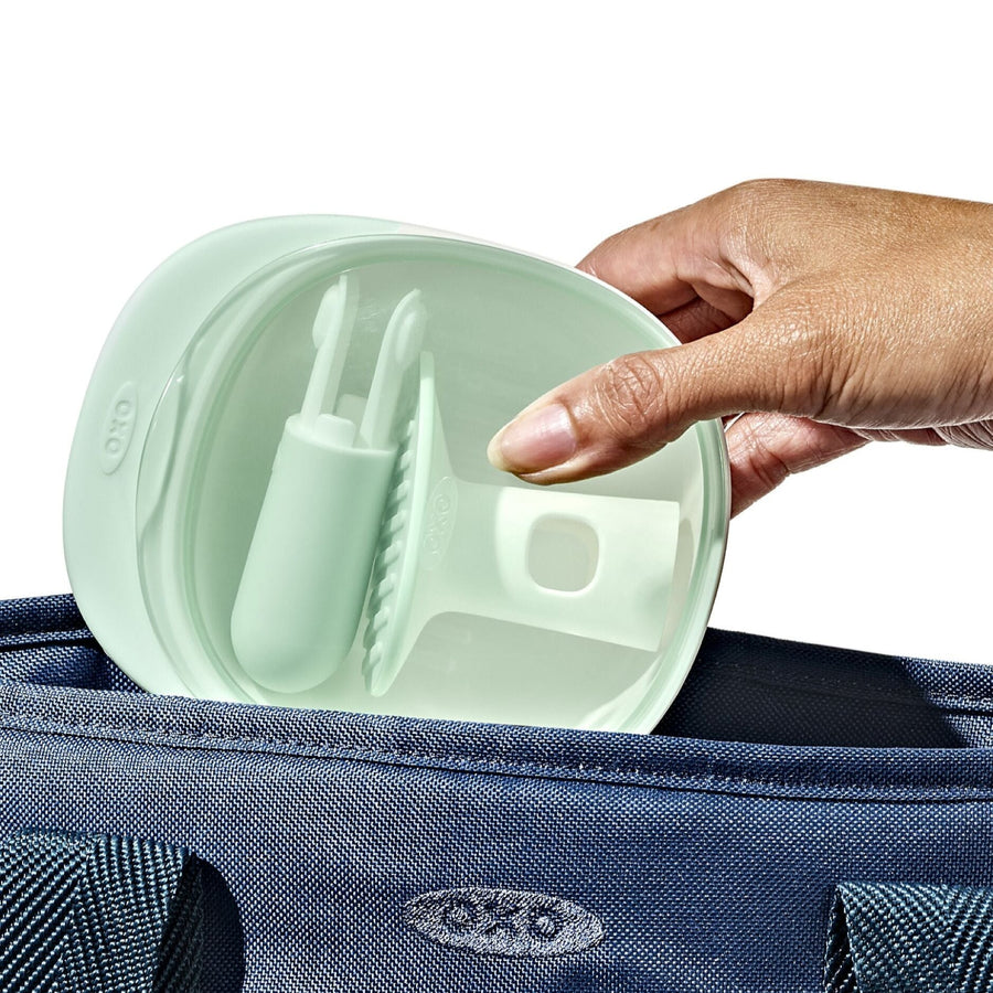 Hand holding a light green silicone lid over a blue bag with a visible brand logo.