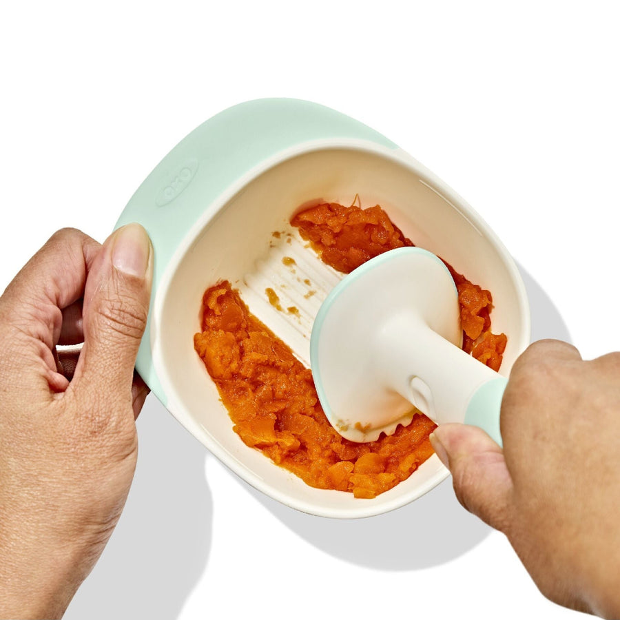 Person using a baby food puree maker with orange puree inside on a white background