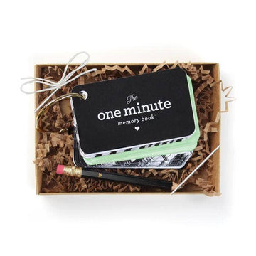 Picture of the One Minute memory book and black mini pencil with brown crinkly paper shreds in a brown kraft gift box with a clear plastic lid and a white elastic string tied in a bow