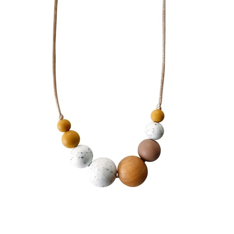 Picture of a teething necklace made of round silicone beads of various sizes in beige and speckled white and a round wooden bead on an ivory satin cord