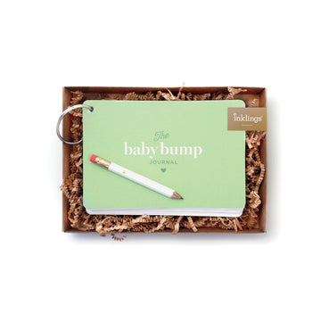 Picture of The Baby Bump Journal with white mini pencil in a brown kraft box with crinkly brown paper shreds on a white background