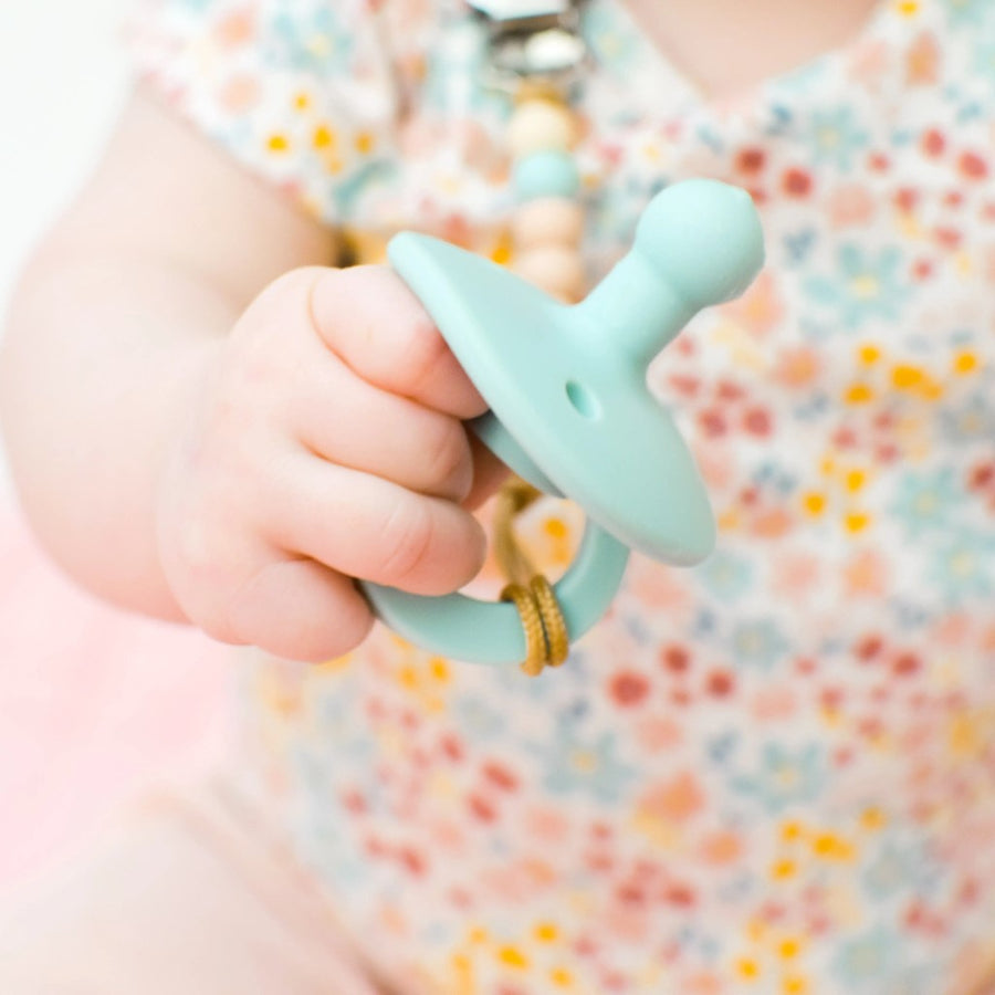 Picture of a close-up of a baby's hand holding a mint colored OLI2 silicone pacifier