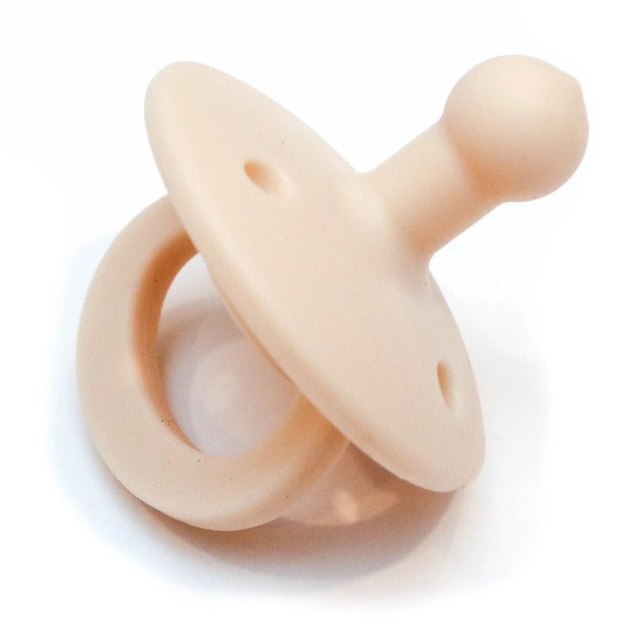 Picture of an OLI2 pacifier in a creamy color. It has a loop handle, a round flange with several holes, and a bulb-shaped nipple