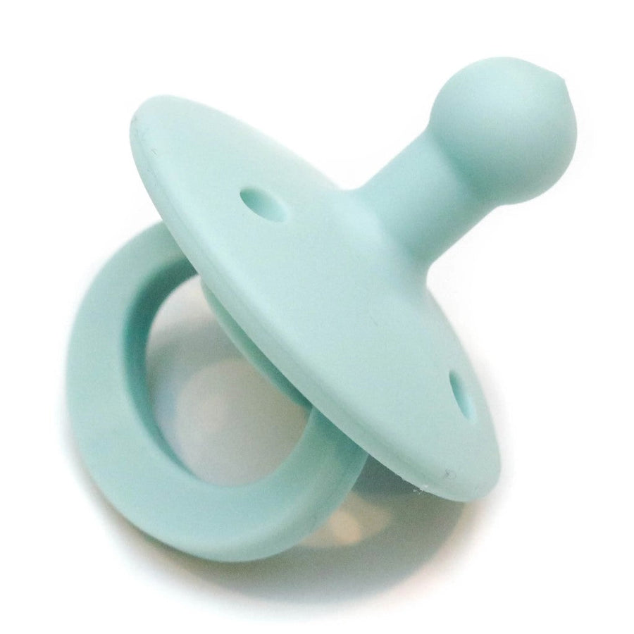 Picture of an OLI2 pacifier in a mint color. It has a loop handle, a round flange with several holes, and a bulb-shaped nipple