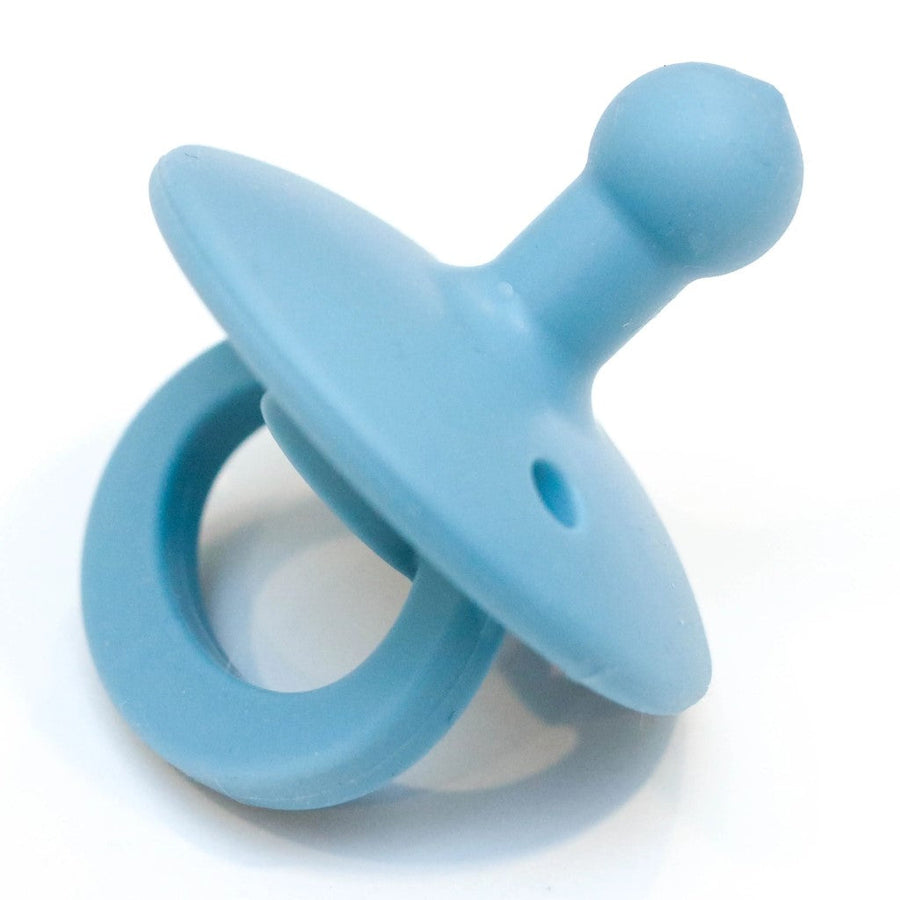 Picture of an OLI2 pacifier in a light blue color. It has a loop handle, a round flange with several holes, and a bulb-shaped nipple