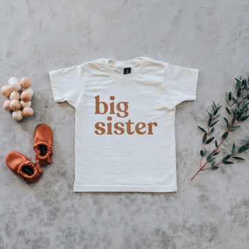 Gladfolk organic cream-colored big sister kids t shirt with camel ink, pictured with booties and wooden clutching toy