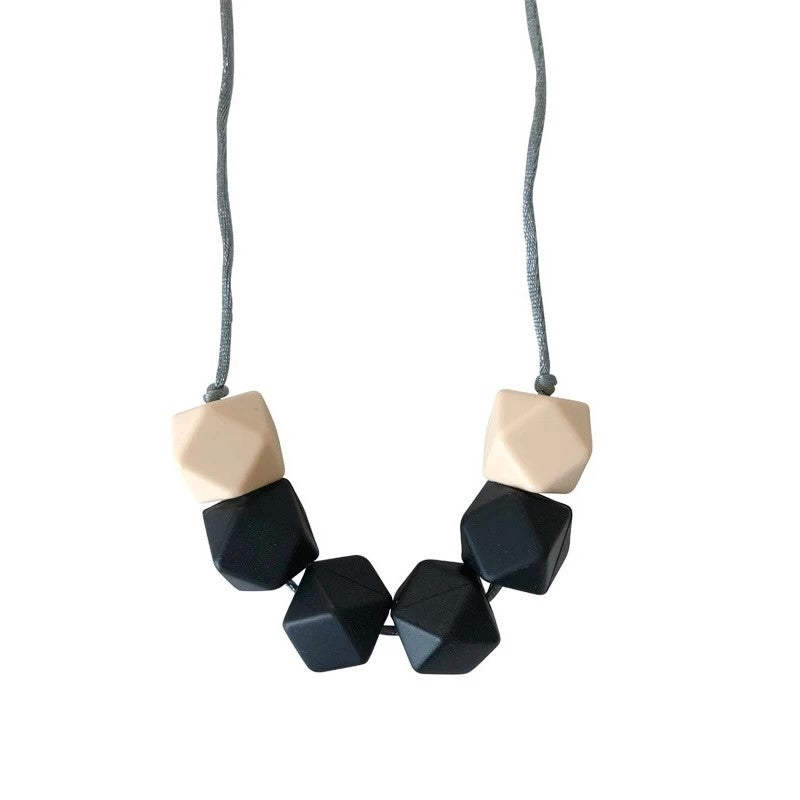 Picture of a teething necklace made of cream and black geometric silicone beads on a gray satin cord